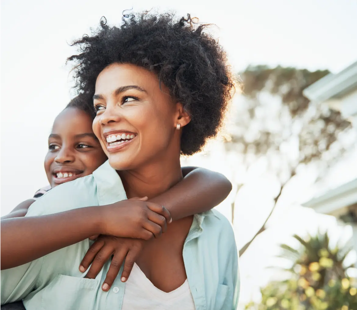 An elderly parent embracing her daughter, both smiling at the camera happily